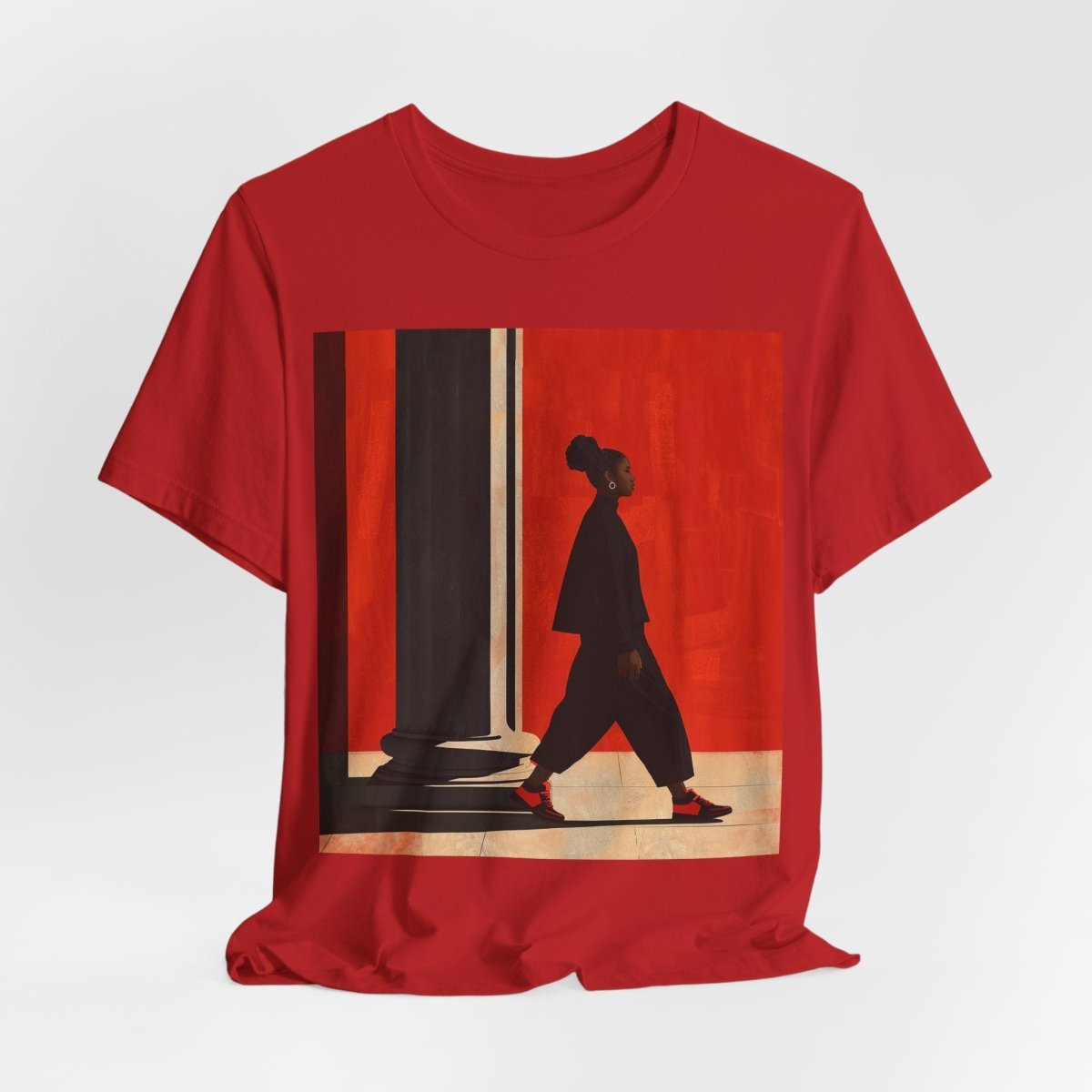 Unisex shirt featuring a Black woman with an afro puff walking past a red wall, dressed in all black with red sneakers.