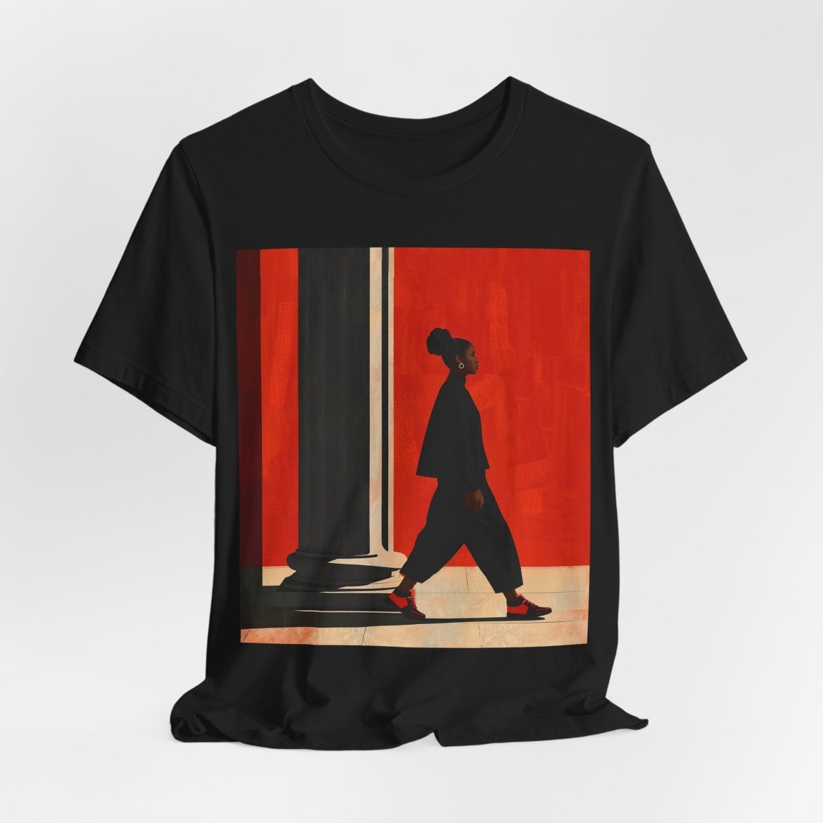 Unisex shirt featuring a Black woman with an afro puff walking past a red wall, dressed in all black with red sneakers.