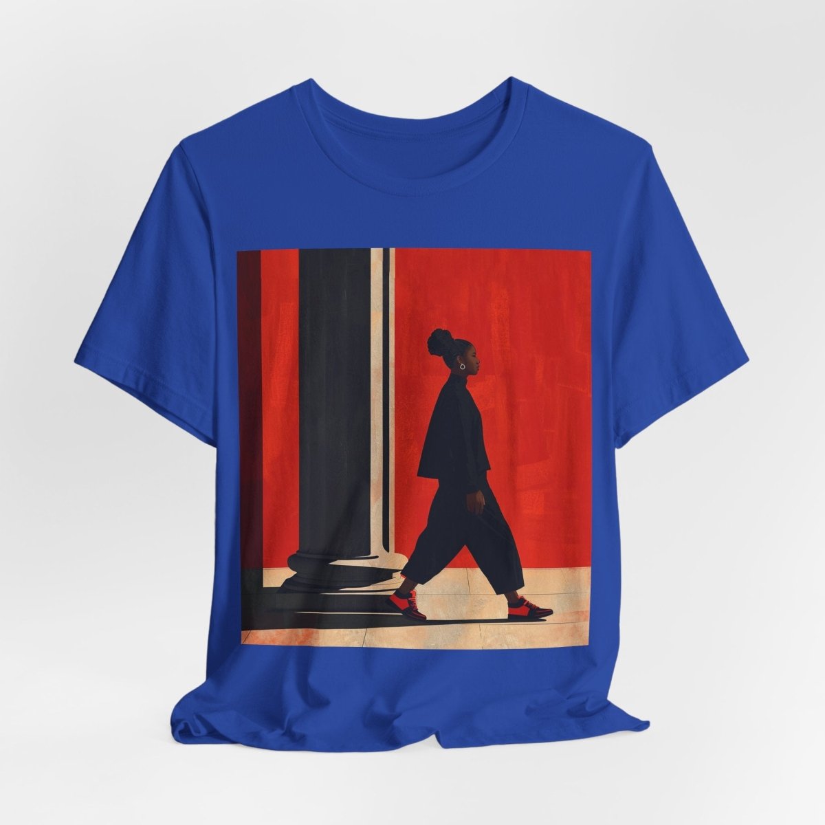 Unisex shirt featuring a Black woman with an afro puff walking past a red wall, dressed in all black with red sneakers.